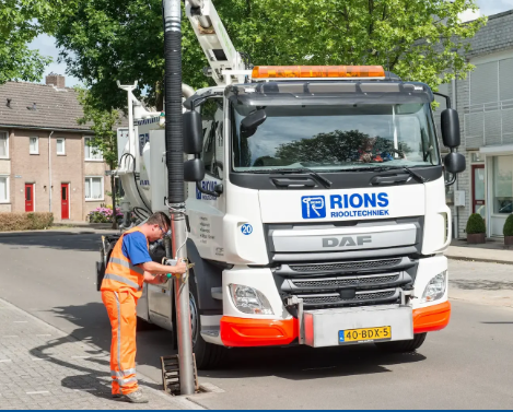 medewerker in oranje werkkleding staat naast vrachtauto met kolkenreiniger aan boord